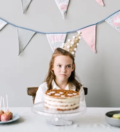 Bambina davanti a una torta di compleanno, con i festoni sullo sfondo